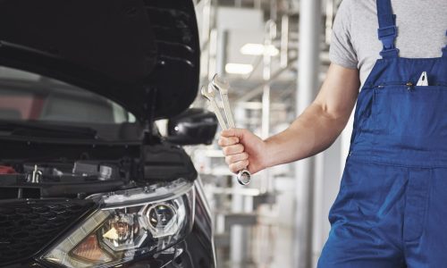 Hands of car mechanic with wrench in garage.